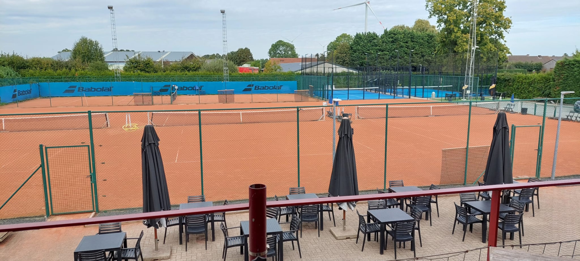 Zicht vanaf het terras over de oranje gravelvelden, met daarachter de blauwe padelvelden en groene hagen.